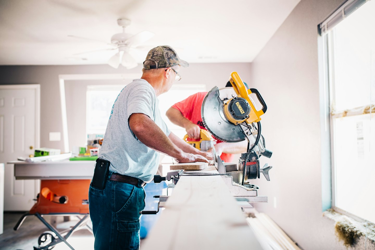Two men working with saws on wood in a room under renovation.