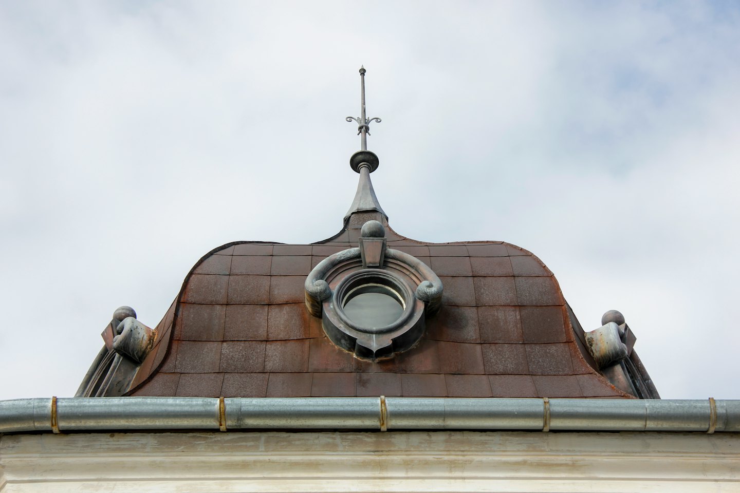 Ornate metal roof with a circular dormer and pointed finial.