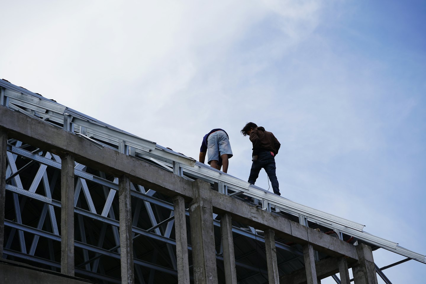 Construction workers install metal roof trusses on a building.